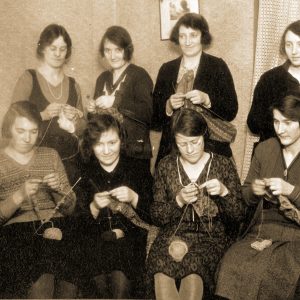 A rectangular Christmas card with a black and white picture of a group of women knitting.